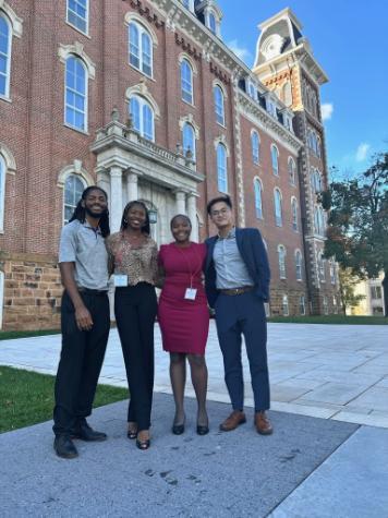 Dr. TehQuin Forbes and three honors students dressed in professional attire standing in front of a University of Arkansas building